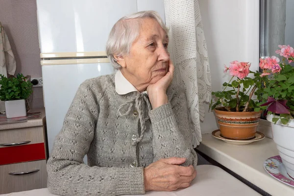 Wanita tua kesepian duduk dekat jendela di rumahnya. — Stok Foto