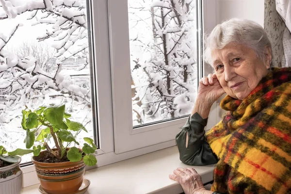 Старая одинокая женщина сидит у окна в его доме. — стоковое фото
