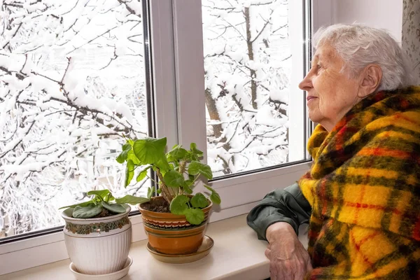 Oude eenzame vrouw zit bij het raam in zijn huis. — Stockfoto