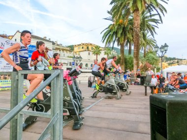 Rapallo, Italy - September 15, 2019: People performing a spinning session outdoors in an urban park of Liguria. Athlets training an their special bikers to keep healthy