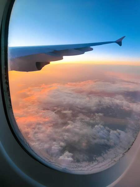 Вид с самолета на голубое небо и белые облака. Летит на самолете. Крыло самолета, летящего над облаками в небе. Окно в овальном. Просветитель.