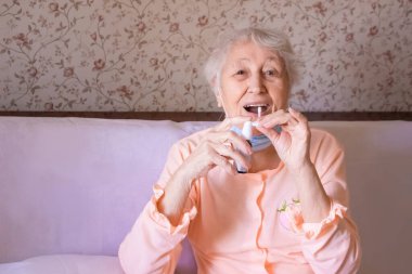 Yaşlı hasta kadın evde öksürük spreyi kullanıyor.