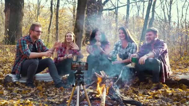 Travel bloggers sitting by fire and recording video with smartphone on tripod — Stock Video