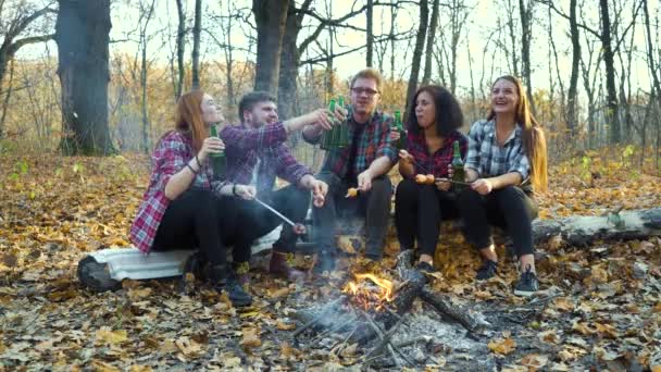 Happy friends menikmati piknik dengan bir oleh api unggun di hutan musim gugur — Stok Video