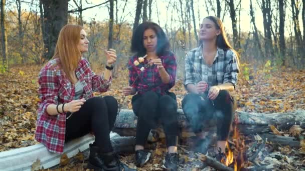 Девушки едят жареный зефир у костра в осеннем лесу — стоковое видео