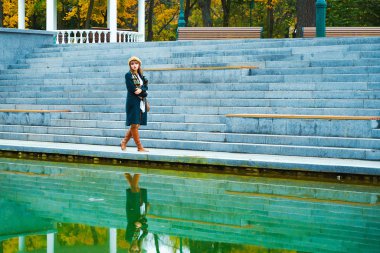 Huysuz kız parkta yürüyor ve göl suyuna yansıyor