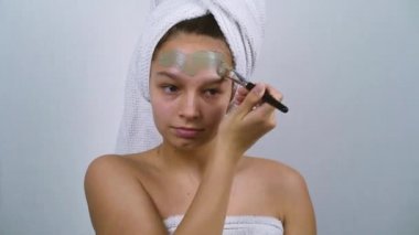 Sivilceli genç bir kız banyo havlularına sarılıp yüzüne kilden maske takıyor.