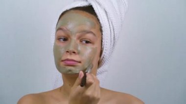 Banyo havlularına sarılı genç kız yüzüne kilden maske takıyor.