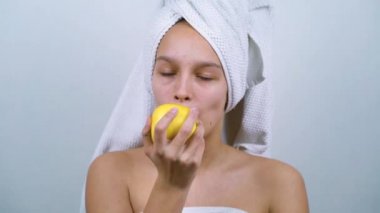 Banyo havlularına sarılı elma yiyen genç kız.