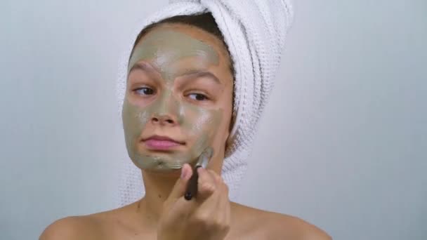 Teenage girl wrapped in bath towels applying clay mask on face — Stock Video