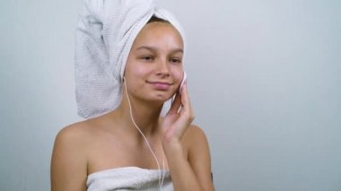 Banyo havluları içinde müzik dinleyen ve yüzünden ekstra krem çıkaran bir genç.