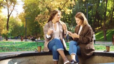 Güzel hippi kızlar sonbahar günü halka açık parkta akıllı telefon kullanırlar.