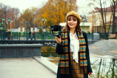 Akıllı telefon ve Steadicam kullanarak parkta video kaydeden güzel bir moda blogcusu