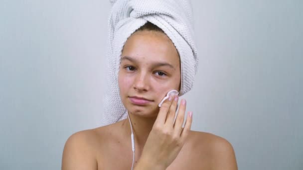 Ragazza adolescente in asciugamano da bagno ascoltare musica e pulizia del viso con batuffolo di cotone — Video Stock
