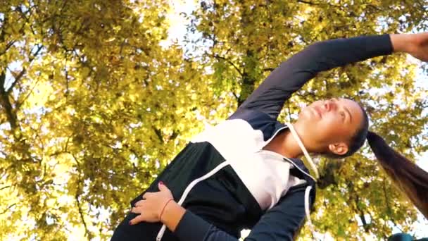 Pretty girl robi ćwiczenia rozciągające pod jesiennymi drzewami — Wideo stockowe