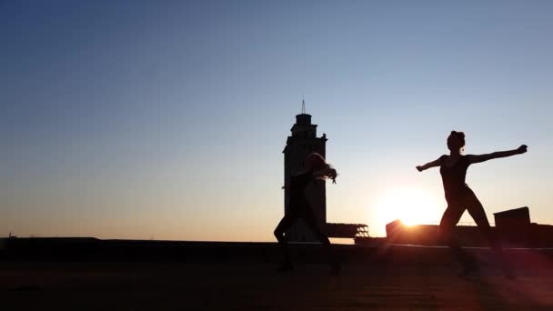 Siluetas de chicas jóvenes bailando al atardecer en el techo — Vídeos de Stock