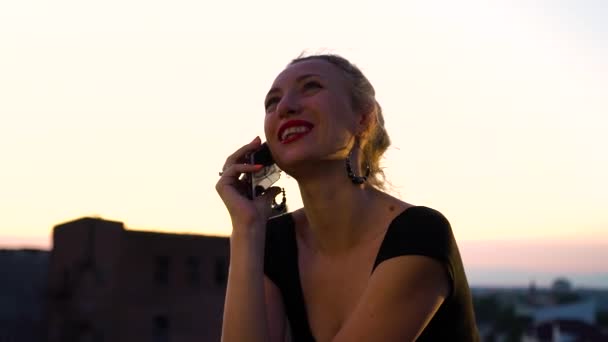 Chica alegre usando teléfono inteligente en el techo al atardecer — Vídeos de Stock