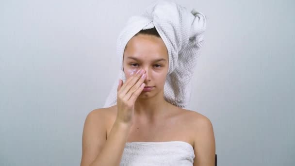 Linda chica envuelta en toallas de baño aplicando crema facial — Vídeo de stock