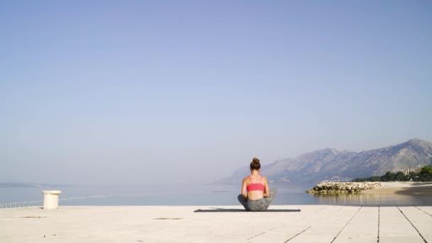 Femme sportive assise dans la pose de lotus sur la jetée de la mer — Video