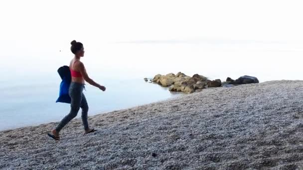 Çakıl taşı plajında yoga dersine yürüyen sağlıklı genç bir kadın. — Stok video
