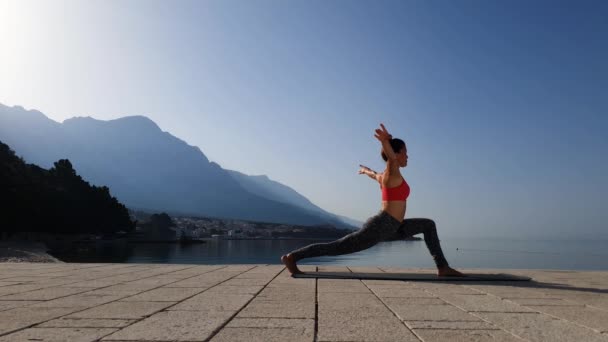 Ragazza che pratica posa guerriero in classe di yoga in riva al mare — Video Stock
