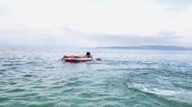 Genç kızlar mavi denizde şişme yatakla eğleniyorlar.