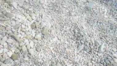 Gri çakıl taşları ve kayalar berrak dalgalı suda deniz yatağında yatıyor.