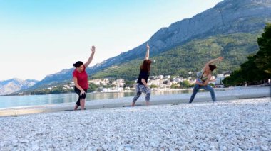 Genç kadınlar yoga dersinde güzel deniz kenarında esniyorlar.