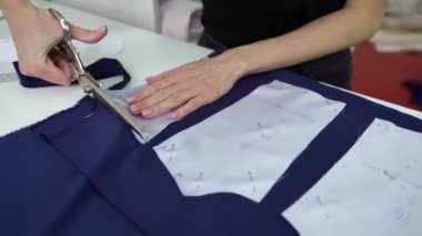 Moda atölyesindeki desenlere göre saten kumaş kesen kadın terzi.