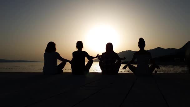 Silhouettes de filles assis dans la pose de lotus de yoga au coucher du soleil sur la jetée de la mer — Video