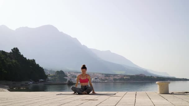 Lovely fit girl sitting in lotus pose on pier by the sea — Stock Video