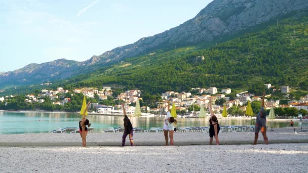 Baska Voda, Croacia - 12 de junio de 2019: cinco atletas haciendo yoga en la playa de guijarros. — Vídeos de Stock