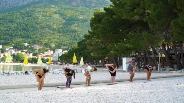 Baska Voda, Kroatië - 12 jun 2019: groep atleten tijdens yogales op het strand — Stockvideo