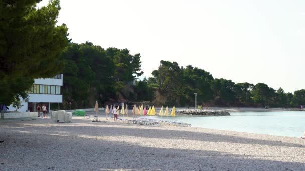 Baska Voda, Chorwacja - cze 12, 2019: turyści spacerujący po plaży z parasolami słonecznymi — Wideo stockowe