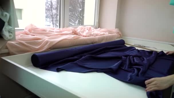 Jeune rouleau écartant femelle de tissu satiné bleu sur la table dans l'atelier de mode — Video