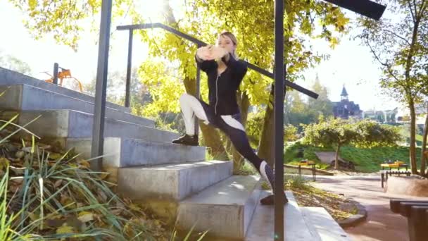 Fit blond meisje in sportkleding stretching op betonnen trap in park — Stockvideo