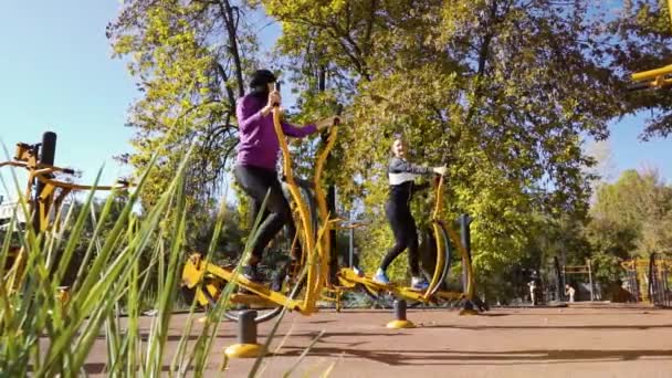 Felices amigos en ropa deportiva ciclismo en bicicletas de ejercicio en el campo de deportes — Vídeos de Stock