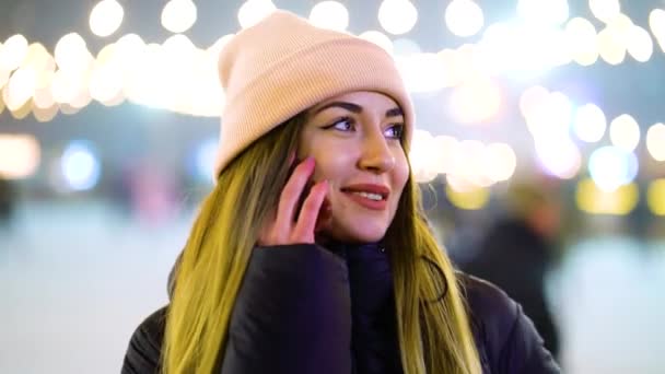 Positive girl in winter outfit talking on phone near skating rink — 图库视频影像