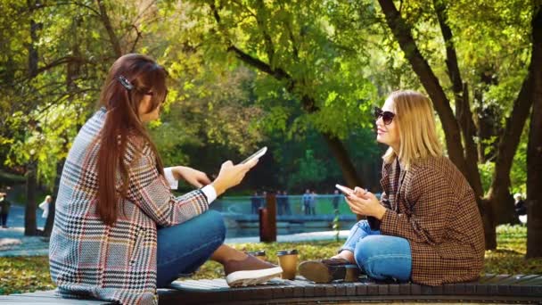 Aantrekkelijke meisjes in hipster outfits surfen social media in de herfst park — Stockvideo