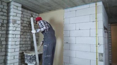 Profesyonel müteahhit havalandırmalı beton duvarda sıva yapıyor.