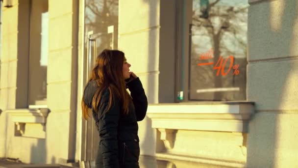 Young girl talking on phone and looking at shop window with sale sign — 비디오