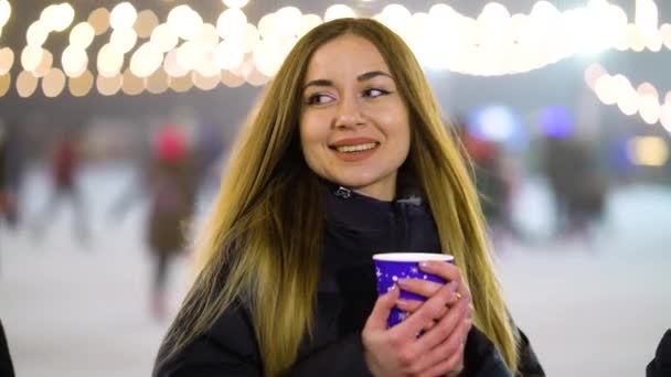 Girl with hot drink standing by skating rink in winter — 图库视频影像