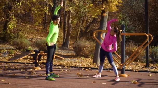 Осенью молодая счастливая семья растягивается на спортивной площадке — стоковое видео