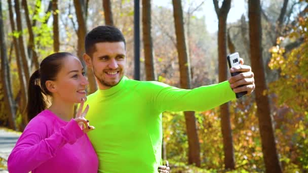Pareja atlética tomando selfie divertido después de correr en el parque de otoño — Vídeos de Stock