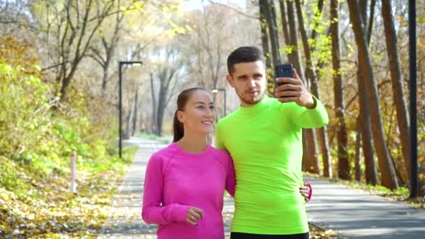 Feliz pareja de bloggers de fitness grabando video en el parque de otoño — Vídeo de stock