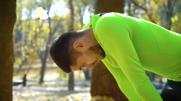 Athletic young man taking break after jogging in autumn park — Stock Video