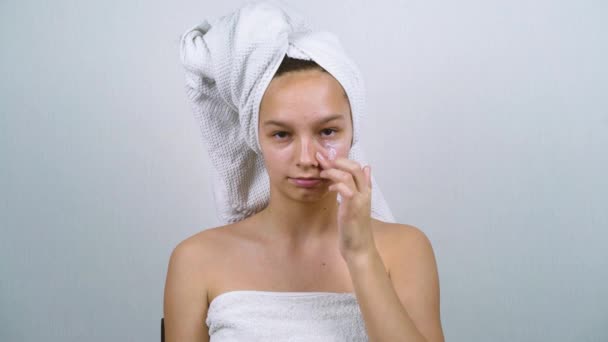Милая девушка, завернутая в белые полотенца, наносит крем для лица после ванны — стоковое видео