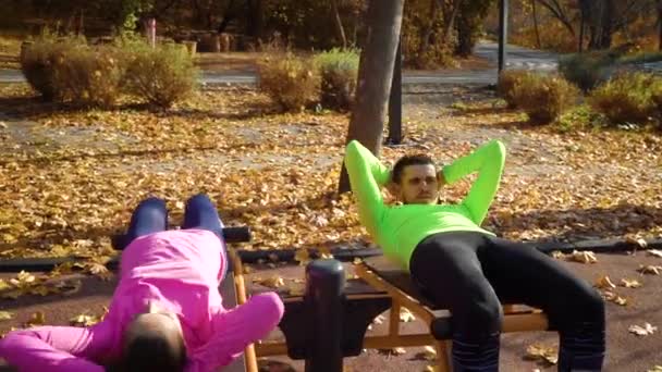 Młoda rodzina robi ćwiczenia brzucha na boisku sportowym jesienią — Wideo stockowe
