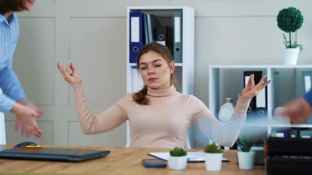 Офисная девушка медитирует на рабочем месте и игнорирует раздраженных коллег — стоковое видео