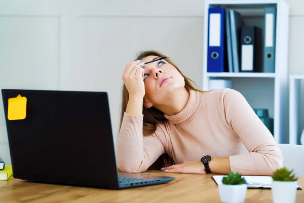 Pretty office girl applying mascara at workplace